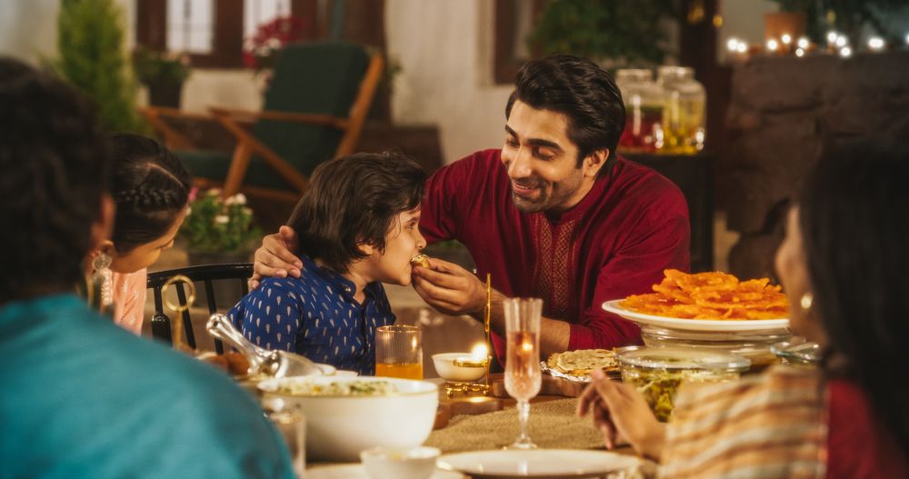 Family Time and Good Happy Memories: Indian Father Feeding his Son and Sharing Traditional Food on a Family Dinner.