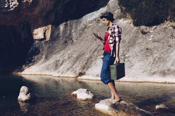 woman standing on rock with case near clear water in lake
