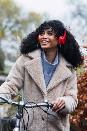 Cheerful Black woman in headphones with bicycle