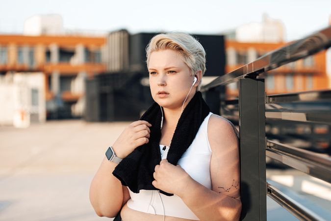 Ahtletic woman leaning on a railing on the roof holding towel