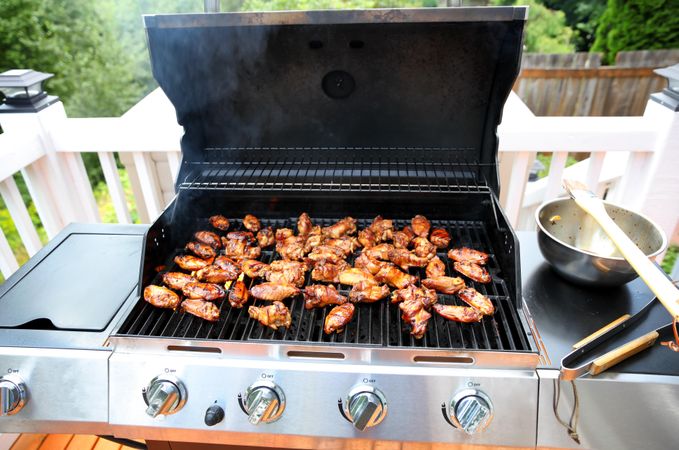 Open barbecue grill cooking hot chicken wings on outdoor deck during summer season