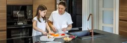 Mother teaching her daughter to cut vegetables for lunch box