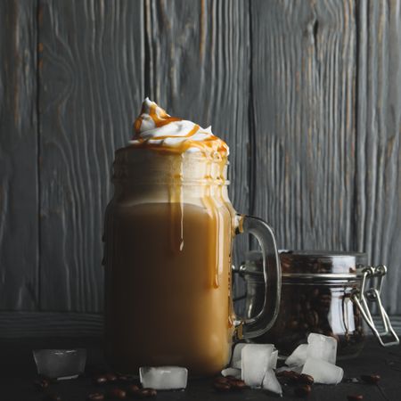 Iced coffee with poured cream on gray wooden background