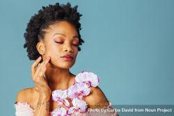 Studio beauty shot of a Black woman with purple flowers and her eyes closed 0Ln8D4