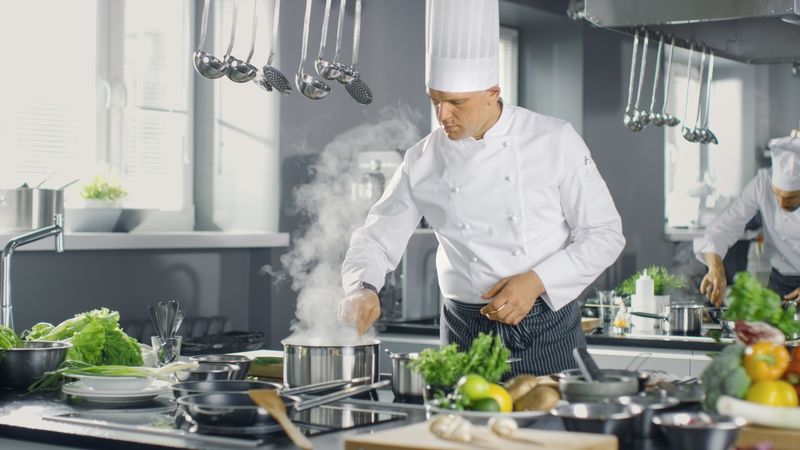 Famous Chef of a Big Restaurant Prepares Dishes with His Help of Cooks. Modern Kitchen is Made of Stainless Steel and Full of Cooking Ingredients.