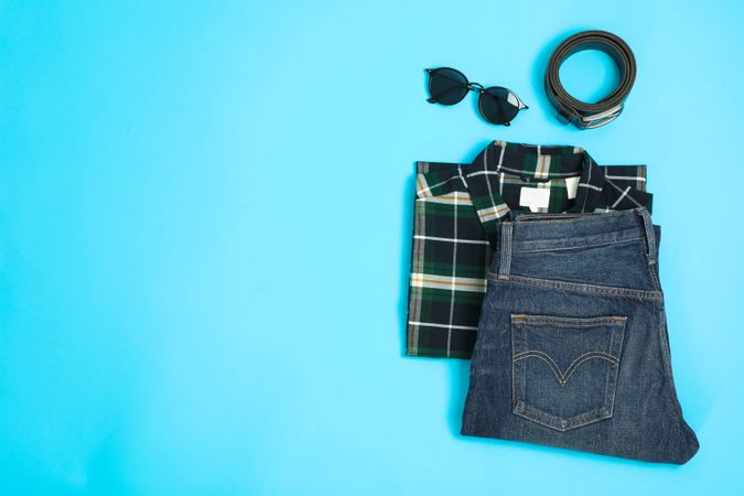 Flat lay composition with shirt, jeans, glasses and belt on color background