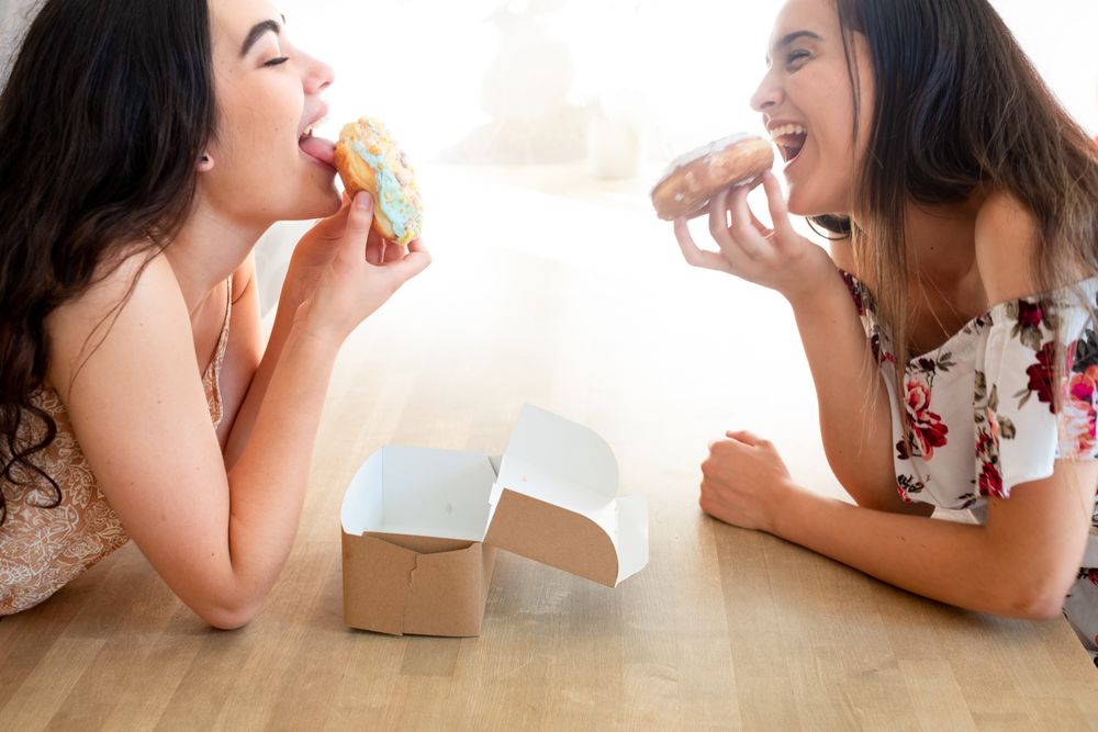 Happy women in sundresses with box of glazed desserts