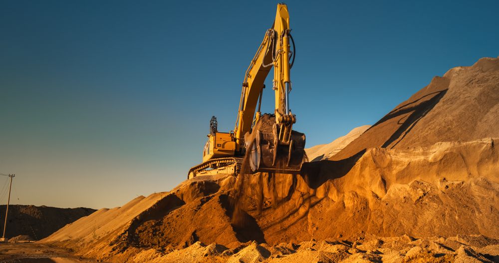 Construction Site On A Hot Sunny Day: Industrial Excavator Digging Sand To Lay Foundation for Building New Apartment Complex. Workers Operating Heavy Machinery To Complete A Real Estate Project.