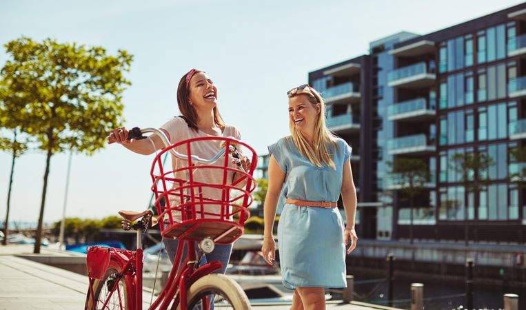 Two laughing women walking with a bicycle along the river walk