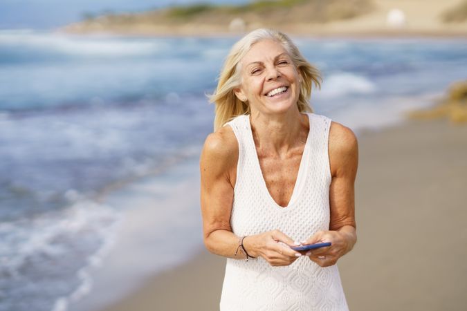 Happy mature female using her phone on a rocky beach