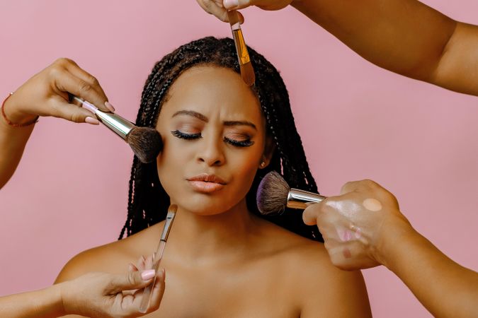 Black woman with eyes closed as hands do her make up