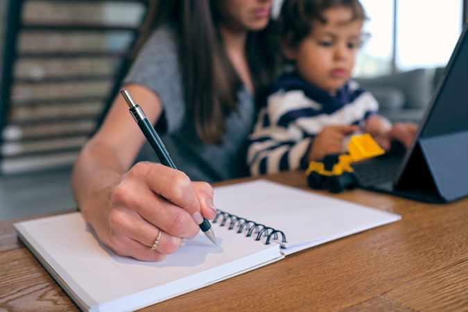 Crop woman sitting with son while working on tablet