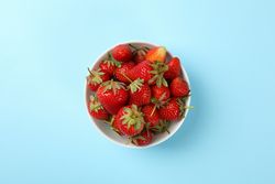 Bowl with tasty strawberry on blue background. Summer berry