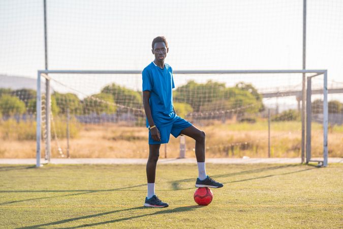Black football player with ball standing on stadium