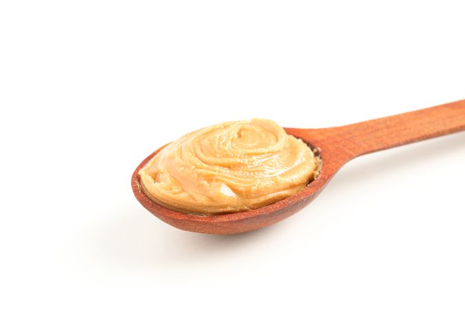 Creamy peanut butter in wooden spoon isolated on bright background, closeup. A traditional product of American cuisine