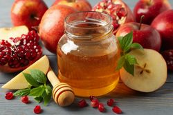 Honey pot surrounded by slices apples and pomegranate on grey table