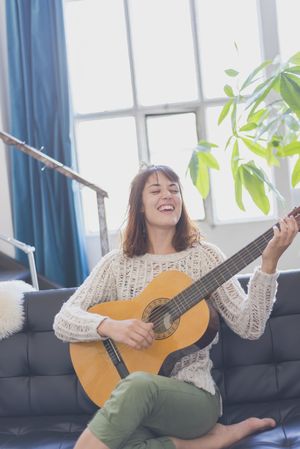 Female singing and playing guitar in living room of bright loft
