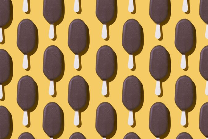 Chocolate popsicle lined up in neat order on a yellow background