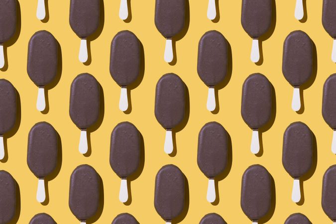 Chocolate popsicle lined up in neat order on a yellow background