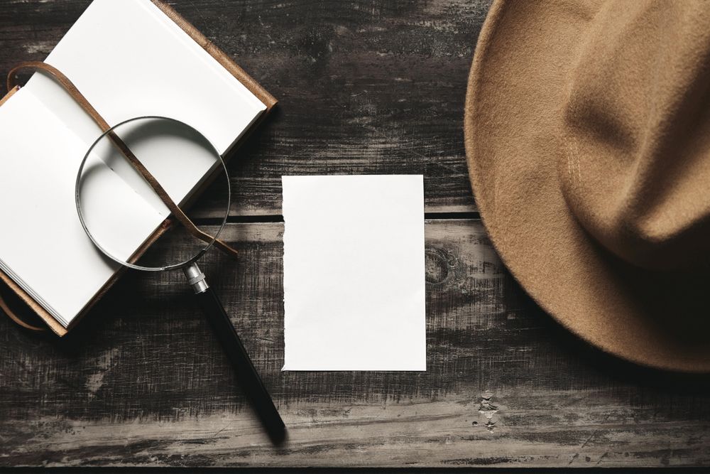 Open notebook, hat magnifying glass on wooden table
