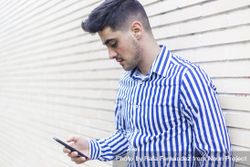 Young happy man leaning on house wall while using his smartphone 4ZeENx