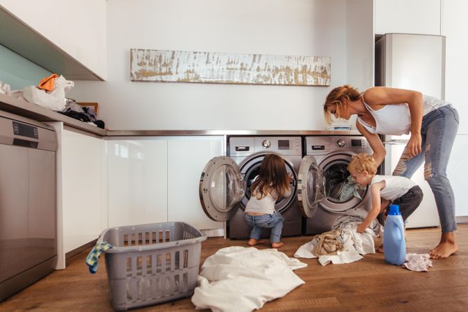 Mother and children putting laundry into washing machine at home