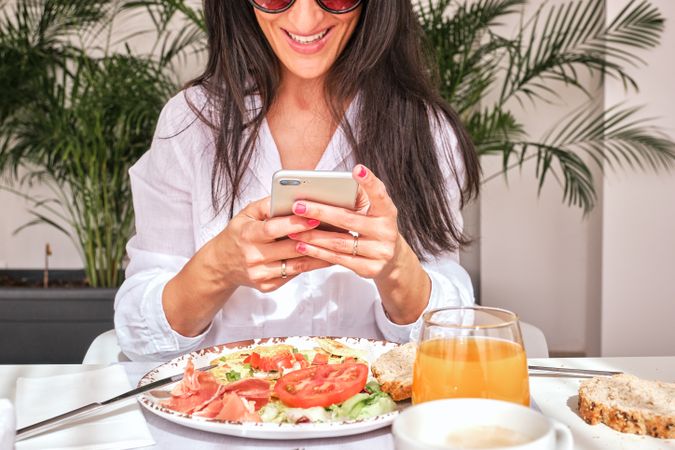 Cheerful woman sitting on table with lunch and reading message i