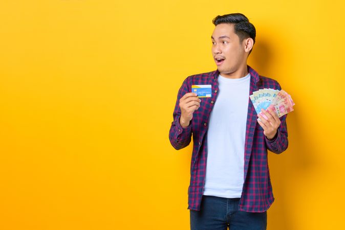 Surprised man looking away while holding credit card and cash