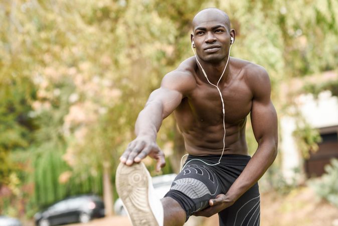 Athletic male stretching lower body with shirt off listening to music on headphones