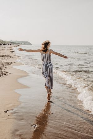 Back view of blonde woman in striped jumpsuit running on seashore