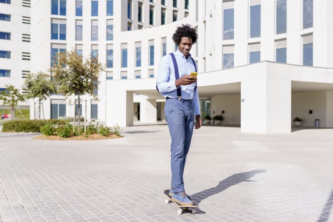 Smiling man on skateboard checking phone outside office