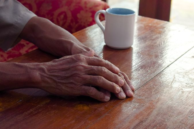 Hands of person resting on table with coffee cup