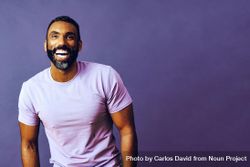 Smiling male in purple studio with hands in pocket, copy space bxk8X4