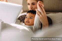 Little boy with mother enjoying watching cartoon movie on laptop while lying in bed 4NalD5