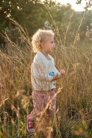 Content little girl carrying Easter eggs in lush meadow