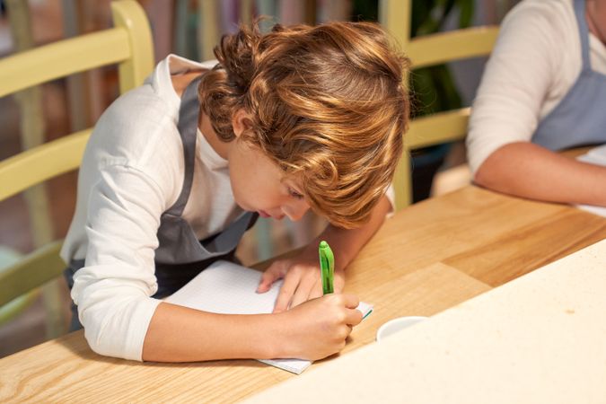 Boy writing on paper in kitchen
