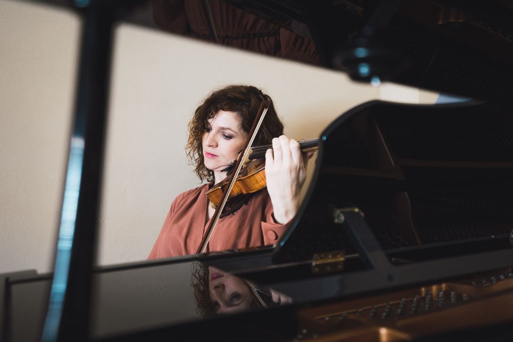 Pregnant woman playing on violin near piano in room