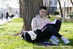 Young man leaning back on a tree and reading a book 48Bl1Z