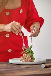 Crop woman decorating steak tartar with green leaves