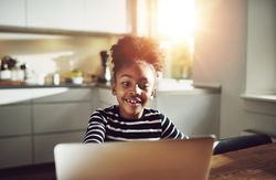 Shot of happy girl working on laptop in sunny room