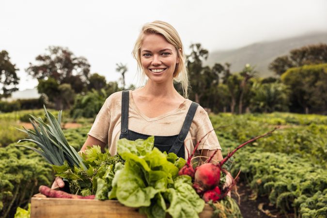 Happy young woman holding a box full of freshly picked produce from her organic vegetable garden