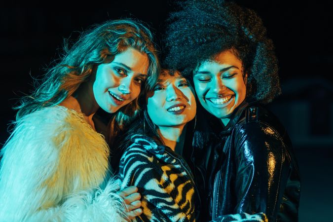 Group of happy female friends lit in green blue light at night