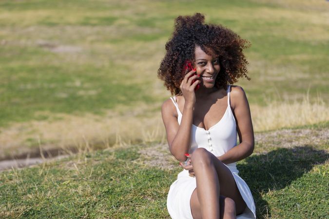 Female in light summer dress sitting in park having pleasant conversation on her phone