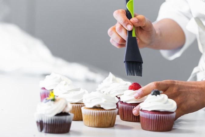 Crop cook smearing berries on cupcakes with syrup