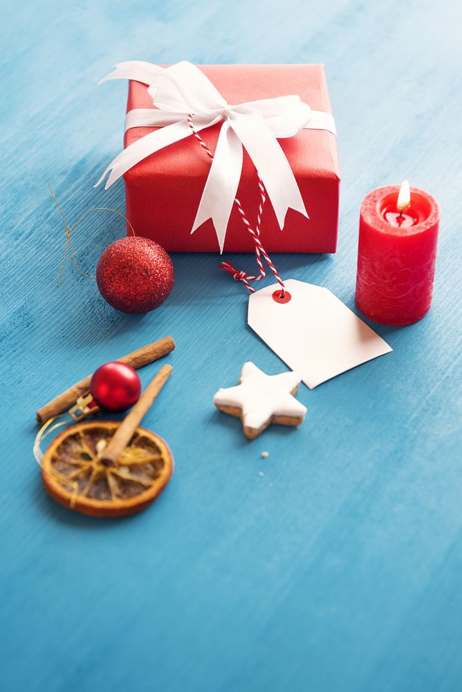 Red gift box with tag on table with cinnamon and a candle