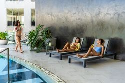Two female friends are lounging in a fancy hotel pool area, laughing and enjoying themselves while waiting for their other friend to join them.