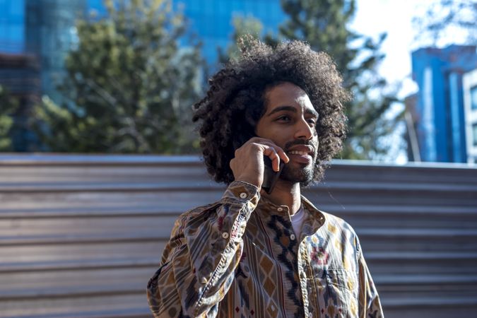 Handsome smiling man with curly hair talking on a mobile phone while standing outdoors