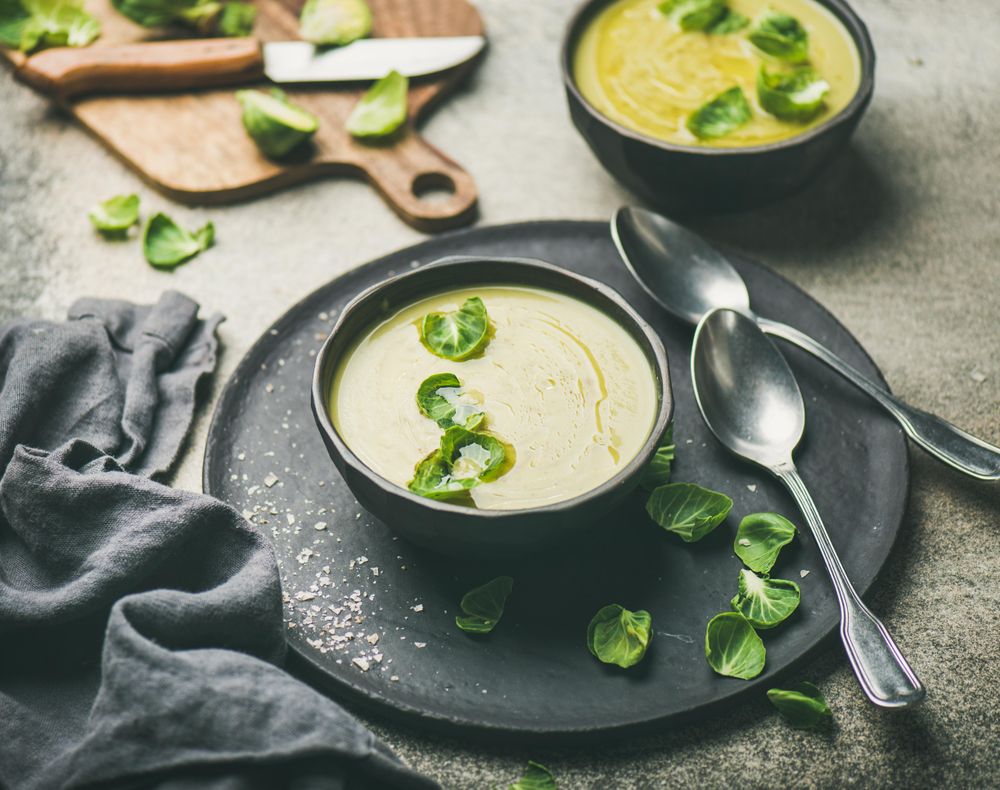 Brussels sprout soup, on dark plate, garnished with fresh sprouts, next to wooden board