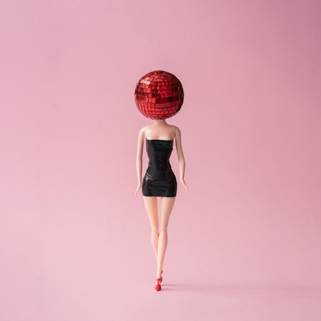 Barbie like doll in dark dress with red disco ball head with pink background