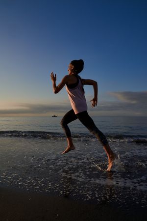 Woman running on wet seashore on evening time